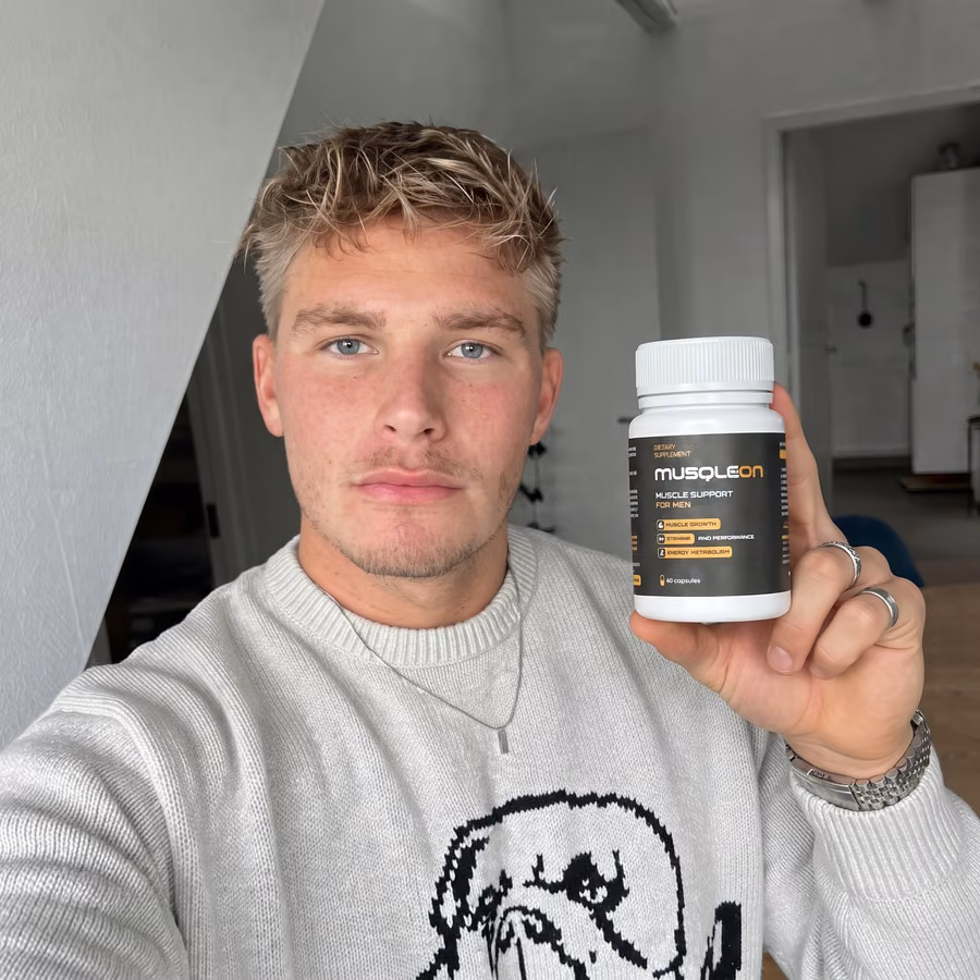Jeune homme blond en pull blanc se prenant en photo avec un flacon de Musqleon